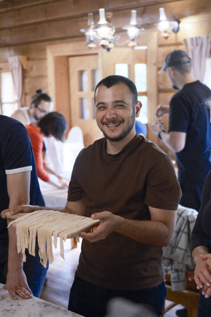 A smiling itrinity team member holding a board of freshly made tagliatelle during Rob's pasta course